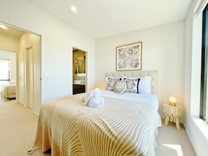 A hotel room with a large bed, a bedside table with a lamp, a window, and a bathroom visible through an open door.