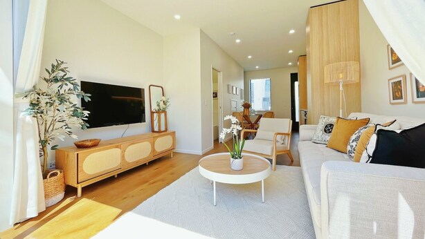 Ein modernes Wohnzimmer mit Fernseher, Holzschrank, rundem Couchtisch und einer Couch mit Kissen.