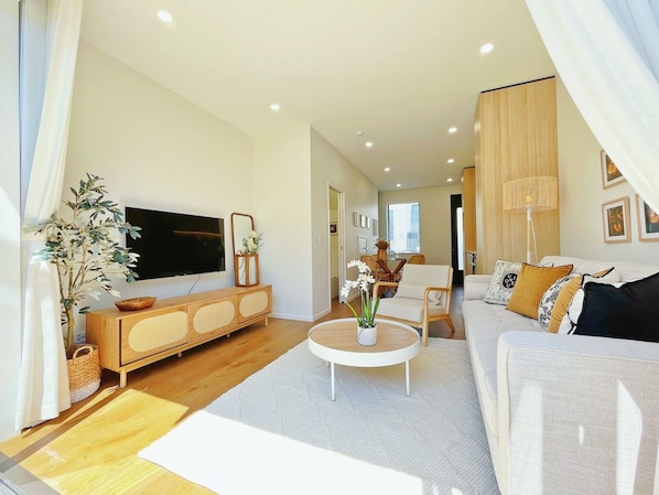 A modern living room with a flat-screen TV, a wooden cabinet, a round coffee table, and a sofa with cushions.