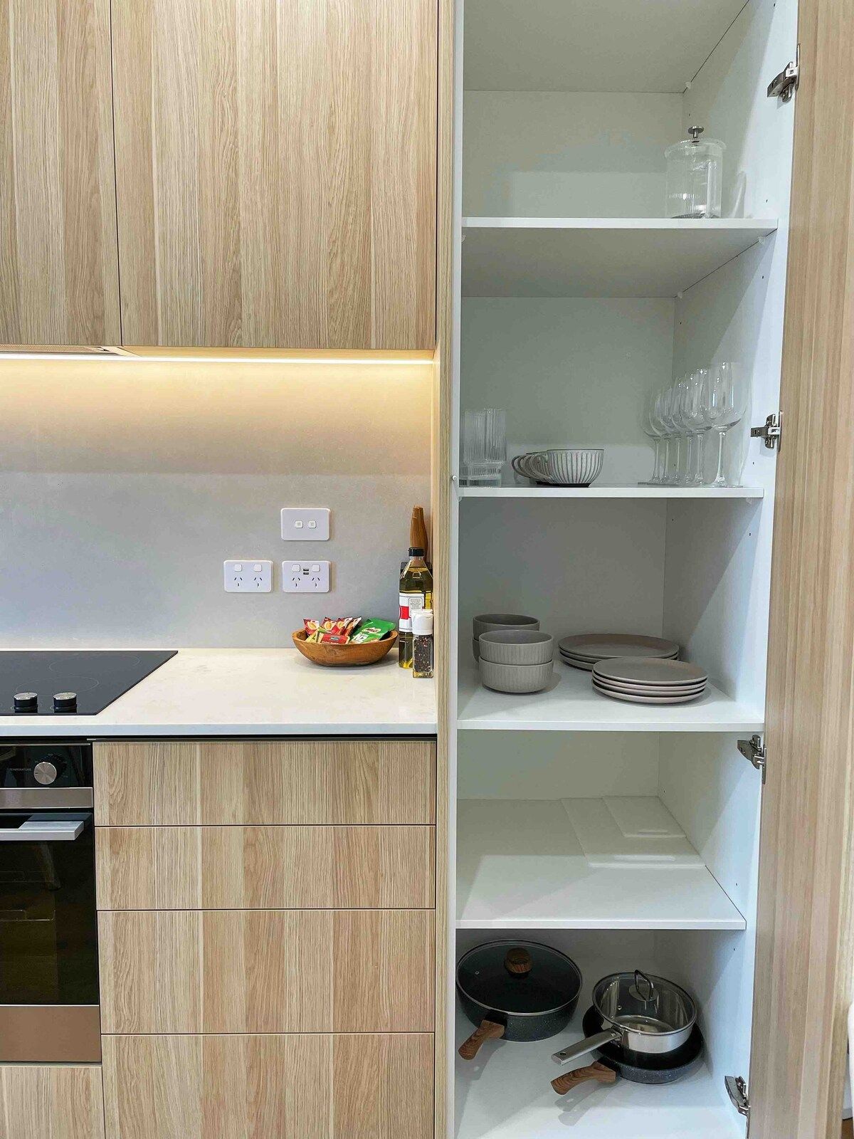 A modern kitchen with wooden cabinets, a built-in oven, and a countertop with a bowl of snacks.