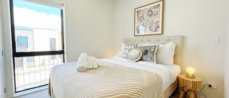 A bedroom with a bed, a bedside table with a lamp, a window, and a wall-mounted picture.
