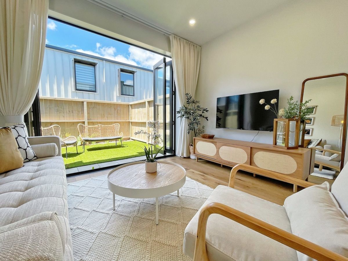 Un salon moderne doté d’un grand téléviseur, d’un canapé, d’une table basse et offrant une vue sur un jardin grâce à une porte coulissante.