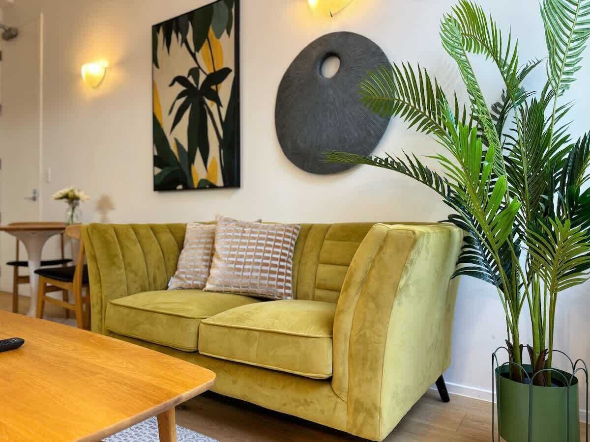 Un salon avec un canapé vert, une table basse en bois, une plante en pot, une œuvre d’art murale et un élément décoratif rond fixé au mur.