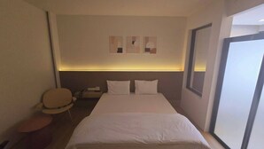 A hotel room with a bed, bedside table, chair, and artwork on the wall. - Rsai sriracha  (Si Racha)