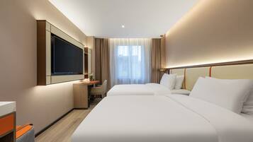 Habitación de hotel con dos camas, un escritorio, televisión y un ventanal con cortinas.
