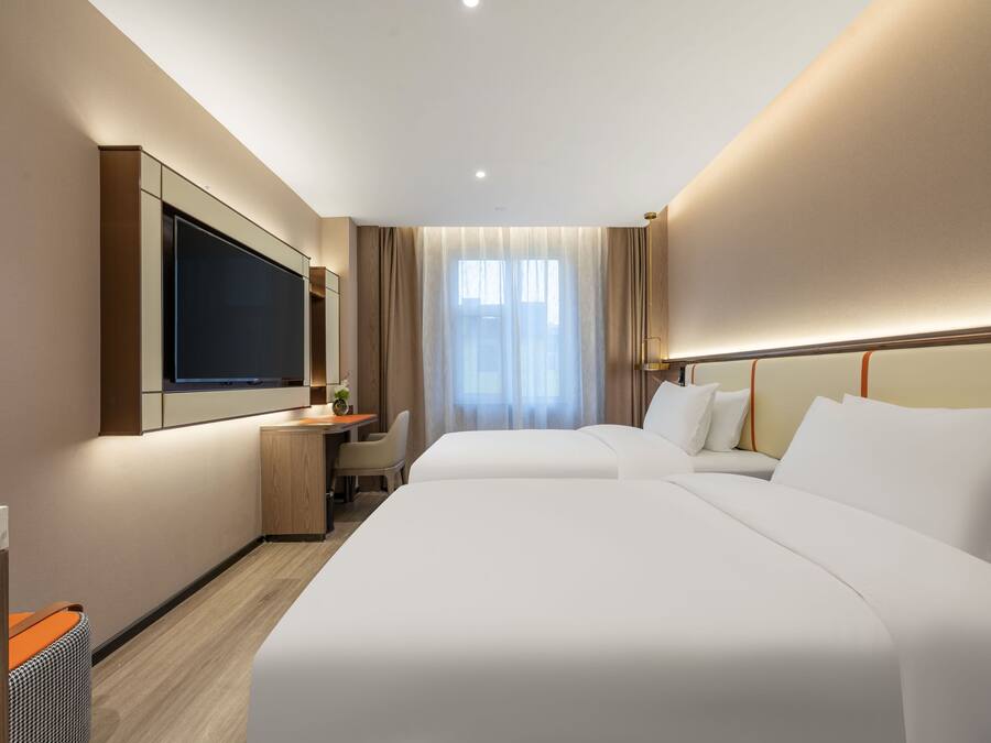 Habitación de hotel con dos camas, un escritorio, televisión y un ventanal con cortinas.