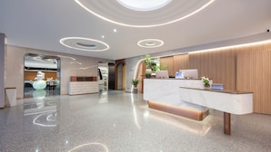 A modern reception area with a marble counter, wooden paneling, and a circular skylight. - WorldHotel Quancheng Sqr Kuanholi Branch (Jinan)