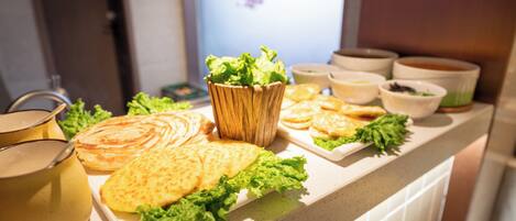A buffet table with various dishes including flatbreads, bowls of soup, and a wooden bowl with lettuce.