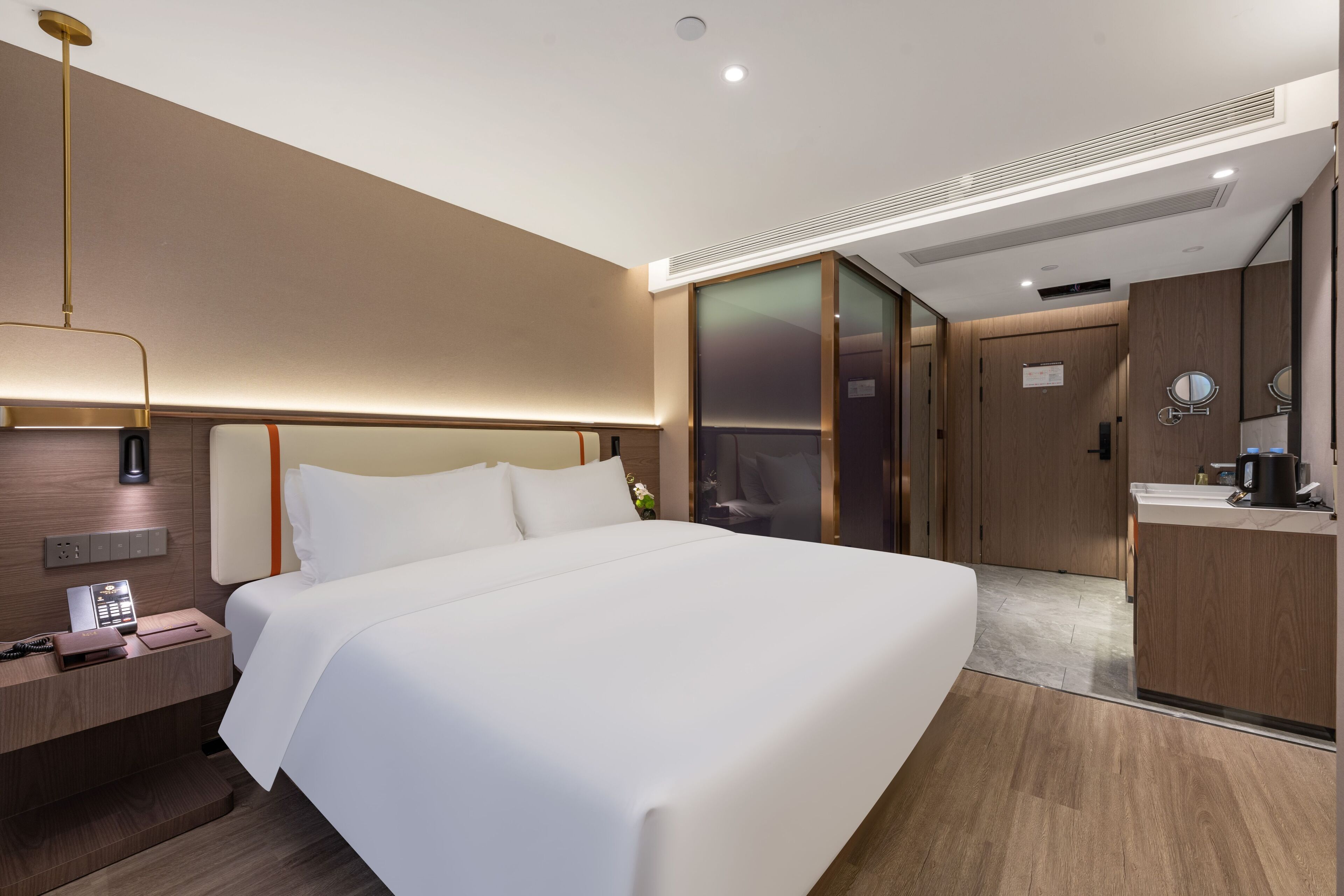 A modern hotel room with a large bed, bedside table with a lamp, a mirror, and a sliding door leading to a bathroom.
