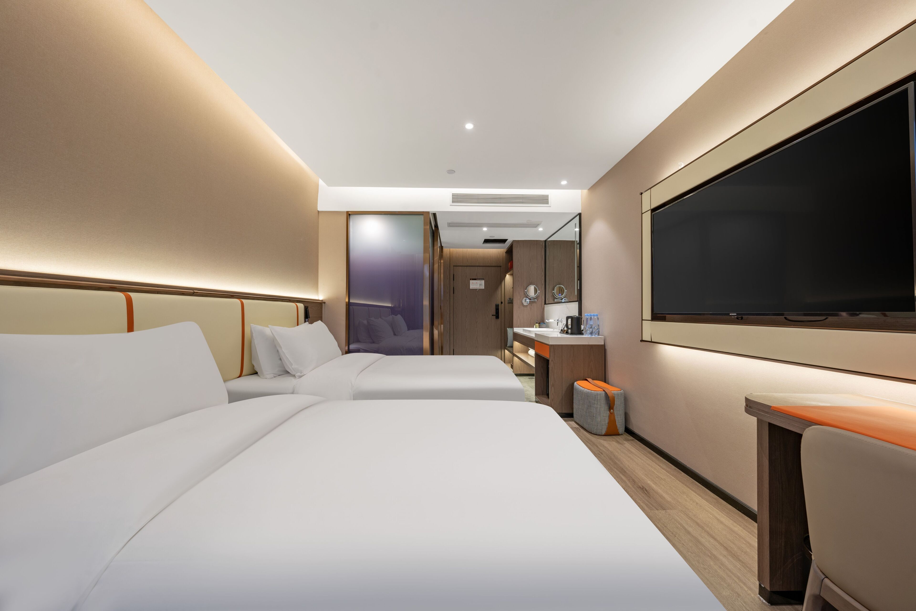 A hotel room with two beds, a desk, a television, and a bathroom visible in the background.