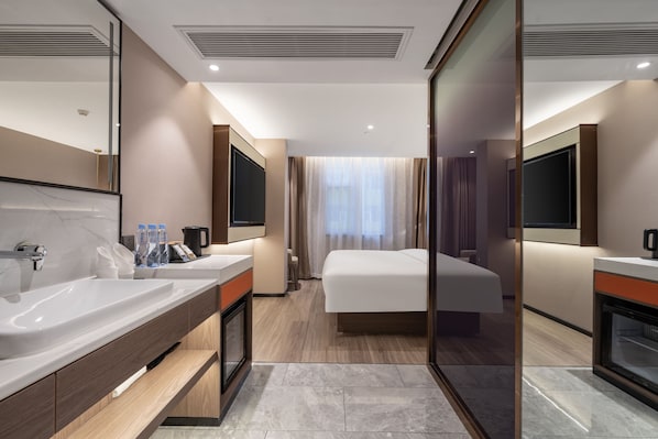 A modern hotel room with a large bed, a separate bathroom with a double sink, and a large mirror.