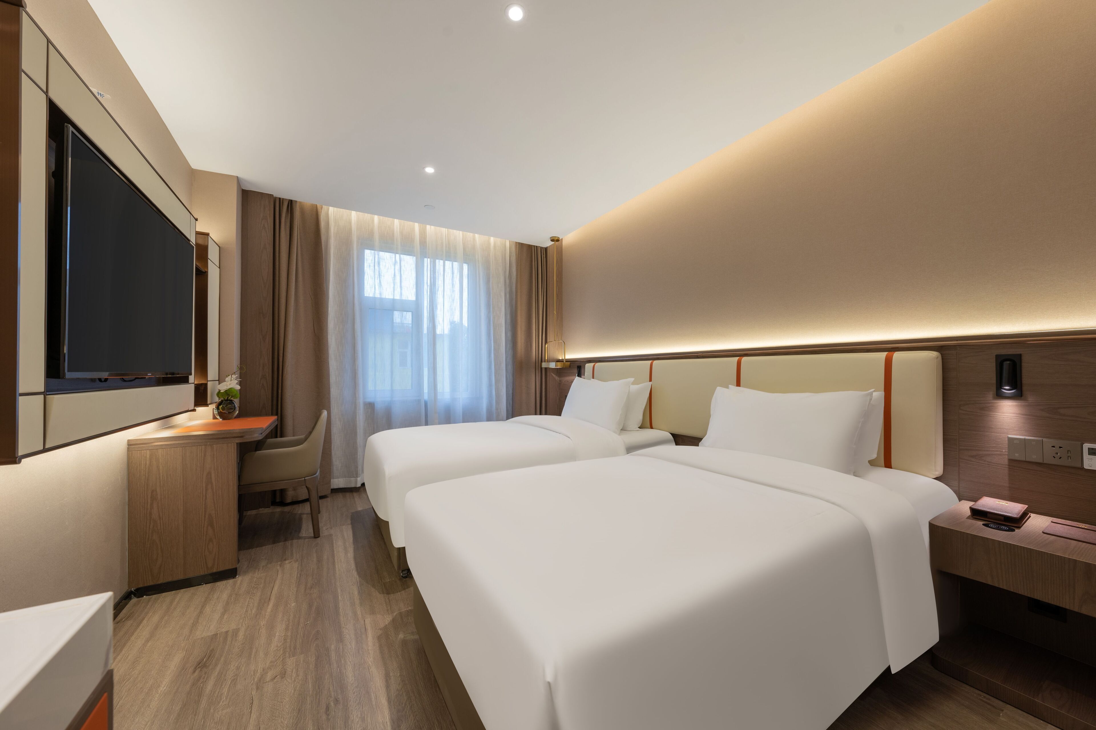 A modern hotel room with two beds, a desk, and a TV.