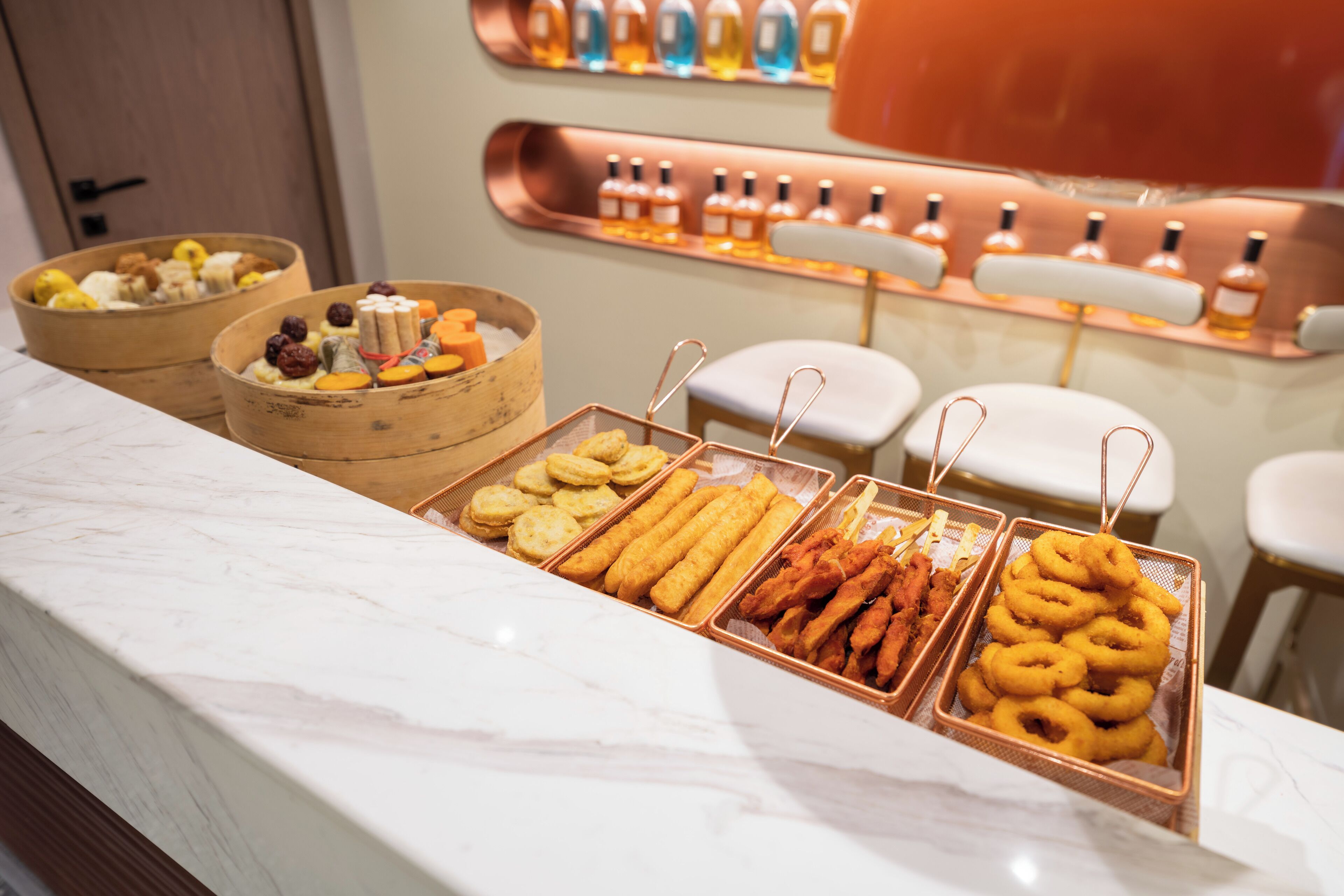 A buffet with various food items and a display of bottles in the background.