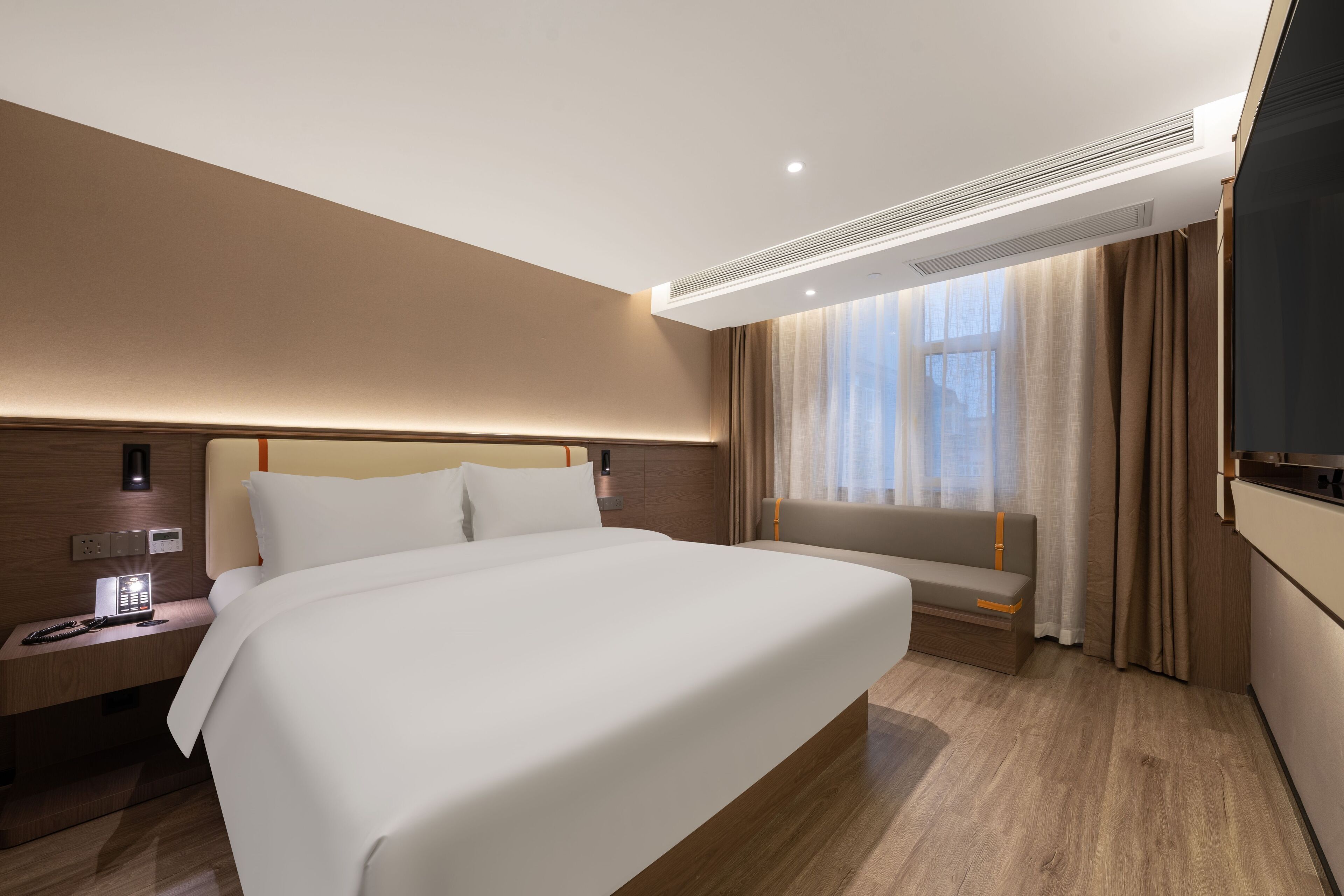 Een moderne hotelkamer met een groot bed, nachtkastje met lamp, ingebouwde televisie en een raam met gordijnen.