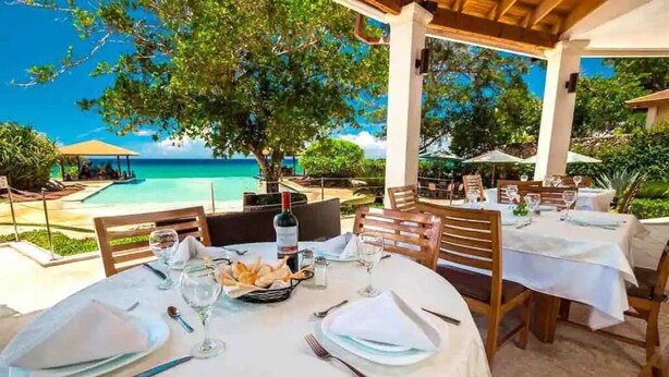 A dining area with tables set for two, overlooking a pool and the ocean. - Luxurious & Charming 3BR VILLA Palmas Del Mar Pool/Jacuzzi/BBQ in lovely Sosúa (Sosúa)
