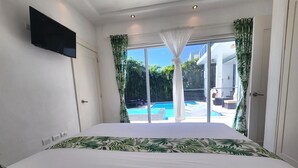 A bedroom with a large bed, a TV mounted on the wall, and a view of a swimming pool through the window. - Luxurious & Charming 3BR VILLA Palmas Del Mar Pool/Jacuzzi/BBQ in lovely Sosúa (Sosúa)