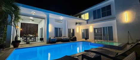 Una casa moderna con piscina, mobiliario de exterior y un patio.