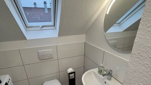 A compact bathroom with a skylight, a toilet, a sink, and a washing machine. - nJoy! Business Apartment Pforzheim (Pforzheim)
