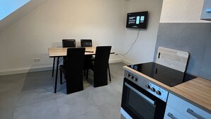 A compact kitchen with a stove, oven, and dining area with chairs and a table. - nJoy! Business Apartment Pforzheim (Pforzheim)