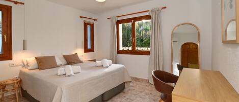 Une chambre à coucher avec un lit, une table en bois, une chaise, un ventilateur de plafond et une fenêtre avec des rideaux.