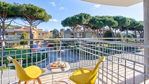 Un balcon avec des chaises jaunes, une petite table ronde et une vue sur un quartier résidentiel, avec des arbres et des immeubles.