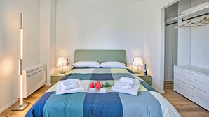 Habitación de hotel ordenada, con cama, lámparas de noche, mesitas de noche, cómoda y vestidor.