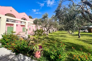 A pink building with a balcony, surrounded by a well-maintained garden with various plants and flowers. - Borgo Primizia T2 Pool And Sea, Otranto, Italy (Otranto)
