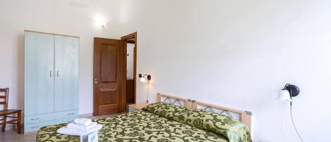 Un dormitorio con cama, armario de madera, mesita de noche, una silla y una lámpara de pared.