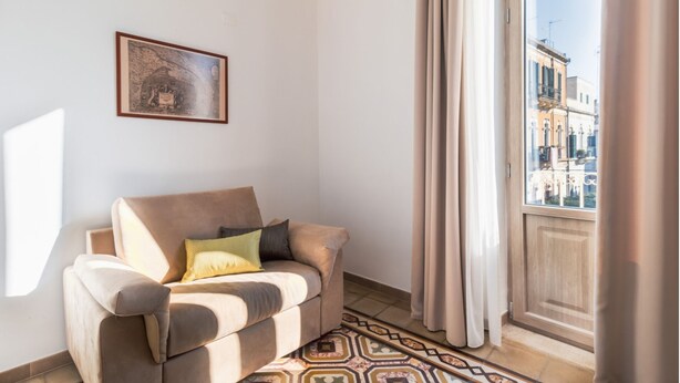 Un salon avec un canapé beige, un tapis à motifs et un tableau encadré accroché au mur.