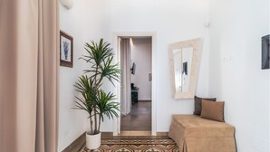 Un couloir avec un sol à motifs, une plante en pot, un canapé beige et un miroir accroché au mur.