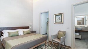 Hotellihuone, jossa on sänky, tuoli, kehystetty taulu sekä kylpyhuone, jossa on pesuallas ja peili.