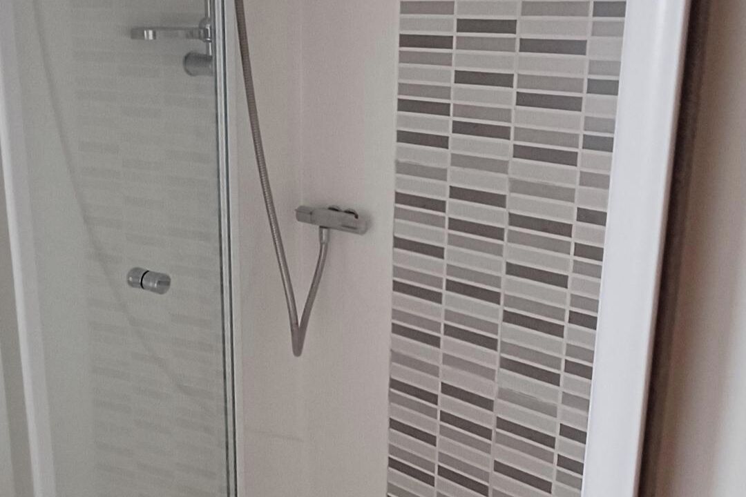 Un espace douche doté d’une porte en verre, d’un pommeau de douche en métal et d’un mur carrelé.