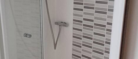 Un espace douche doté d’une porte en verre, d’un pommeau de douche en métal et d’un mur carrelé.