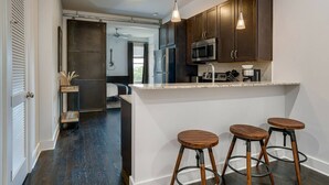 A modern kitchen with dark wood cabinets, stainless steel appliances, and a bar area with stools. - Urban King Loft - Cali King - 8 Min to Broadway! (Nashville)