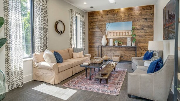 A living room with a beige sofa, a grey armchair, a coffee table, and a patterned rug. There is a wooden accent wall with a painting and a shelf with decorative items. - Urban King Loft - Cali King - 8 Min to Broadway! (Nashville)