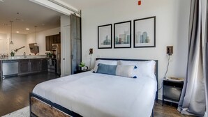 Ein modernes Schlafzimmer mit einem großen Bett, einer Küche im Hintergrund und drei gerahmten Bildern an der Wand.