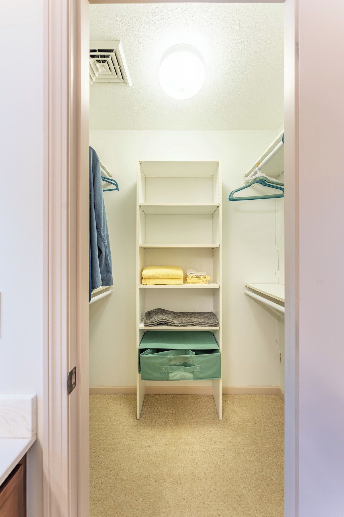 Un vestidor con estantes blancos, una percha y un contenedor verde para guardar objetos.