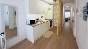 A compact kitchen with white cabinets, a microwave, and a sink. A wooden floor and a mirror are visible.