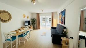 A modern living room with a dining area, a black sofa, a TV, and a balcony with a view.