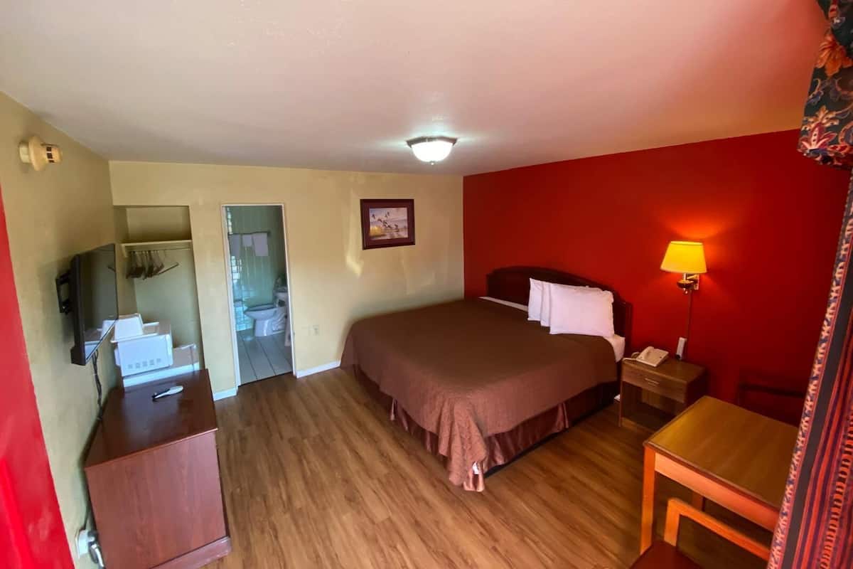 Ett hotellrum med en säng, ett skrivbord, en lampa, en tv och ett badrum som syns genom en öppen dörr.