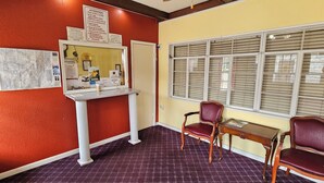 A reception area with a desk, two chairs, a bulletin board with notices, and a window with blinds. - Deluxe Inn (Stuttgart)