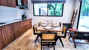 A modern kitchen with wooden cabinets, a dining table set for six, and a view of greenery through the window.