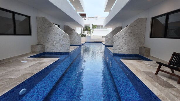 A swimming pool with blue mosaic tiles, flanked by stone walls and benches. - Town Center Zama Condo Hotel by Marea (Tulum)
