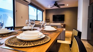 A dining table set with white plates, bowls, and wine glasses, with woven placemats and a ceiling fan in the background. - Town Center Zama Condo Hotel by Marea (Tulum)