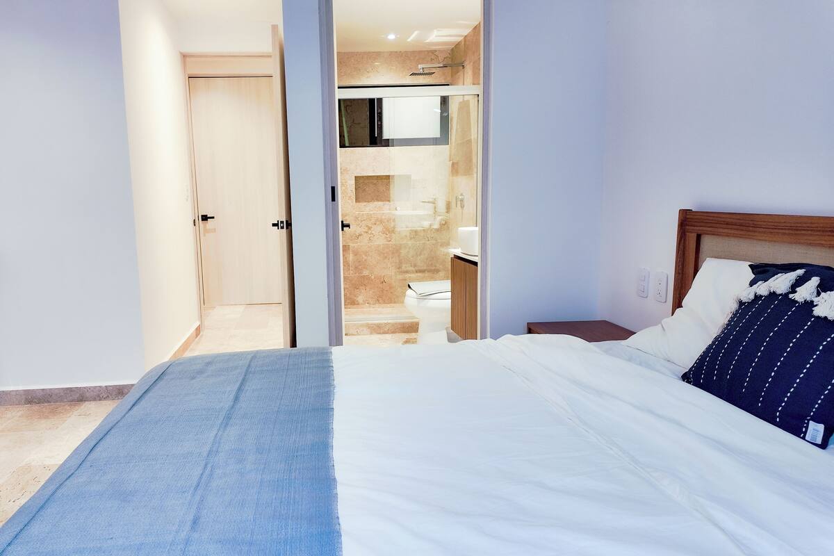A hotel room with a bed, a nightstand, a wooden dresser, and a bathroom visible through an open door.