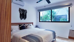 A bedroom with a bed, a window, and a wall-mounted air conditioner. - Town Center Zama Condo Hotel by Marea (Tulum)