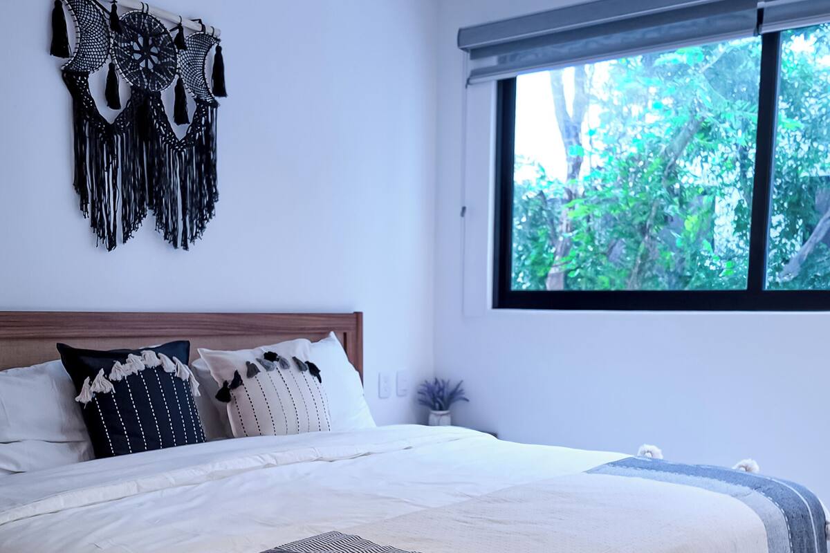 A bedroom with a large bed, a ceiling fan, and a window with a view of trees.