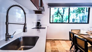 A modern kitchen with a stainless steel sink, a flexible faucet, and a window with a view of trees. - Town Center Zama Condo Hotel by Marea (Tulum)