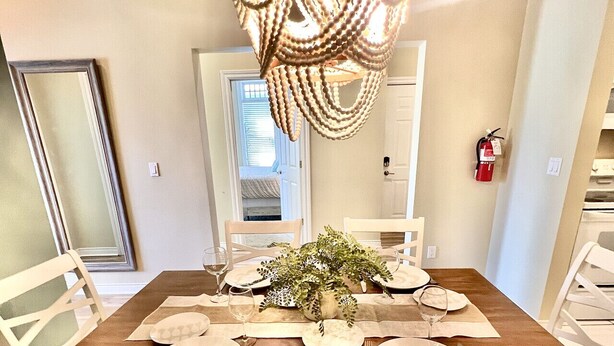 A dining room with a wooden table set for four, white chairs, a chandelier, and a plant centerpiece. - Downtown, Roof Deck, Fireplace (Saugatuck)