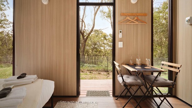 A modern room with a bed, a dining table with chairs, and a view of the outdoors. - Maroota Greens JOY by Tiny Away (Maroota)